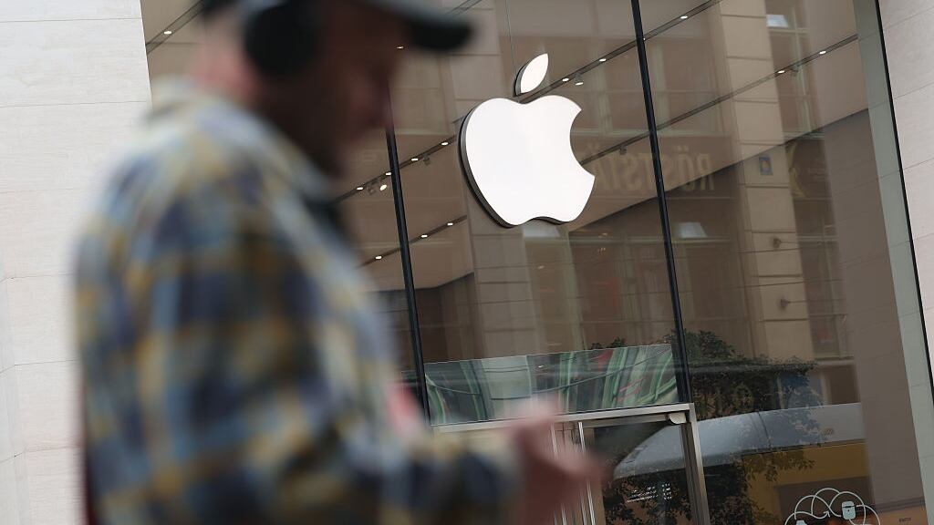 A man with headphones and carrying a smartphone walks past an Apple Store on April 23, 2025 in Berlin, Germany.