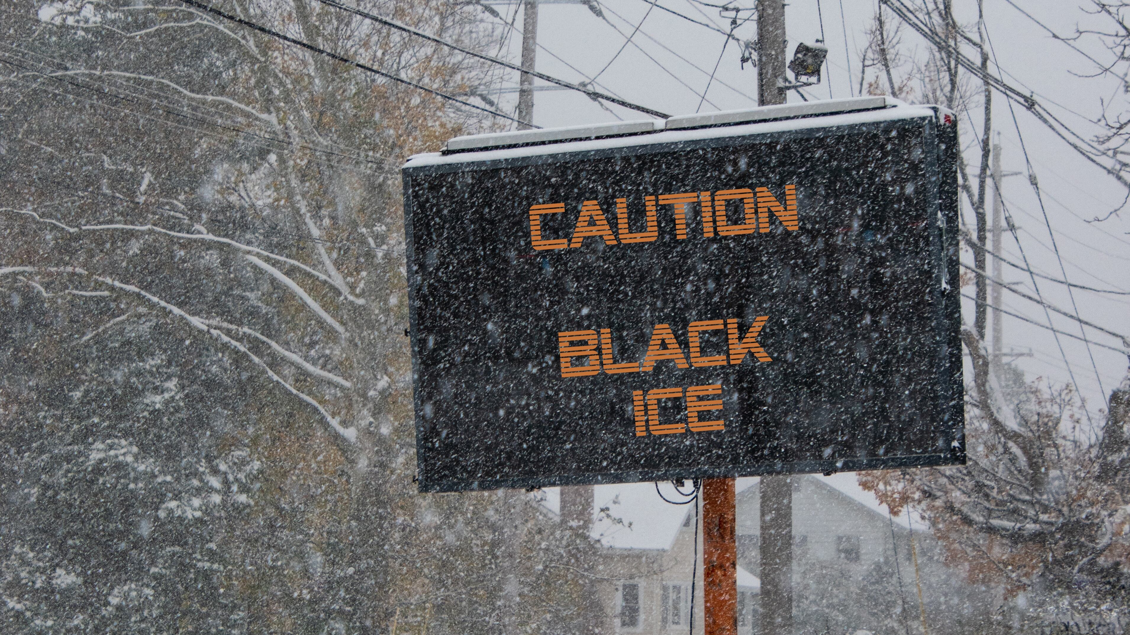 Electric road traffic mobile sign by the side of a snow covered road with snow falling warning of black ice on road
